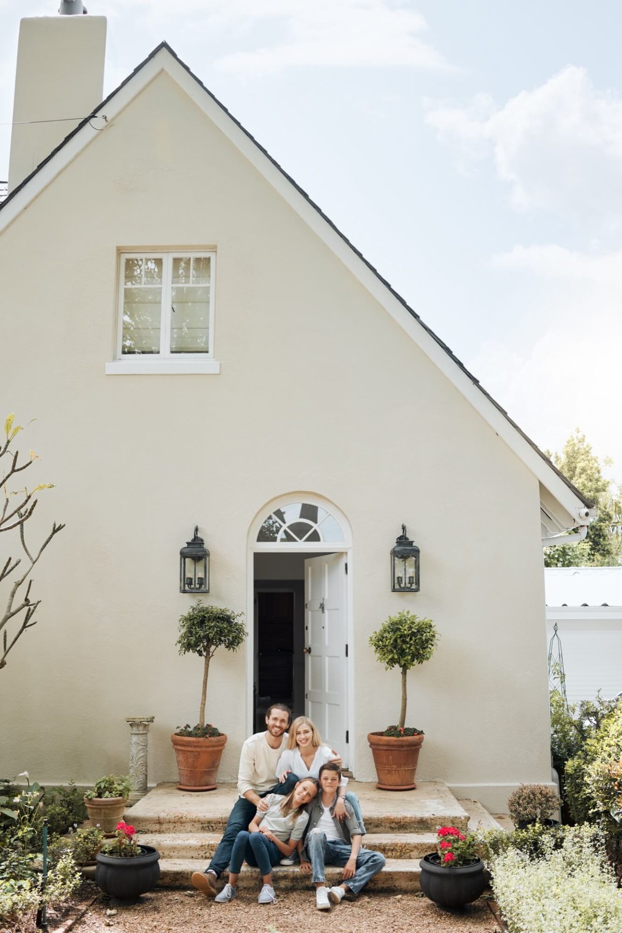 Omgivna av sitt hus med dess nyrenoverade ljusa fasad och de gröna växterna vid entrén, sitter familjen tillsammans på trappan